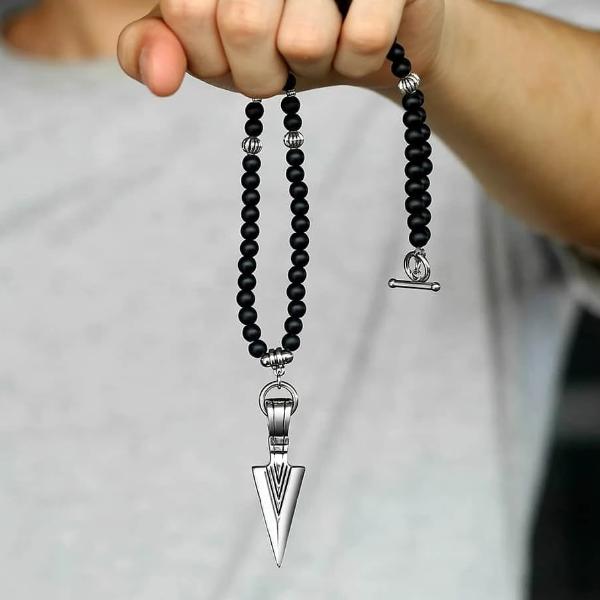 Man holding a black beaded necklace with a silver arrowhead pendant