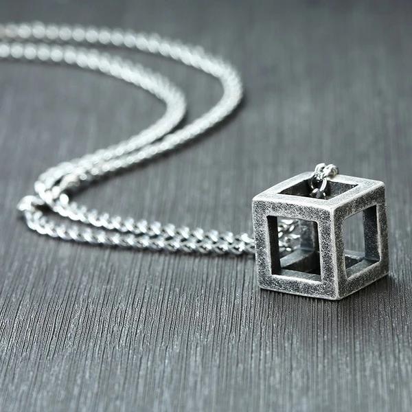 Worn metal cube pendant on a silver curb chain