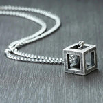 Worn metal cube pendant on a silver curb chain